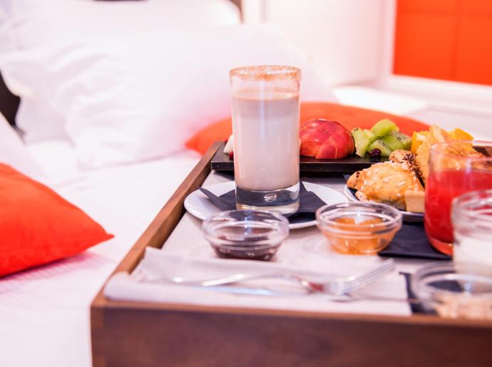 Colazione a letto con frutta, dolci, e bevande su un vassoio.