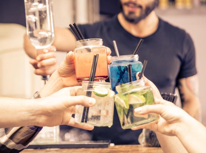 Amici brindano con cocktail colorati in barattoli di vetro.