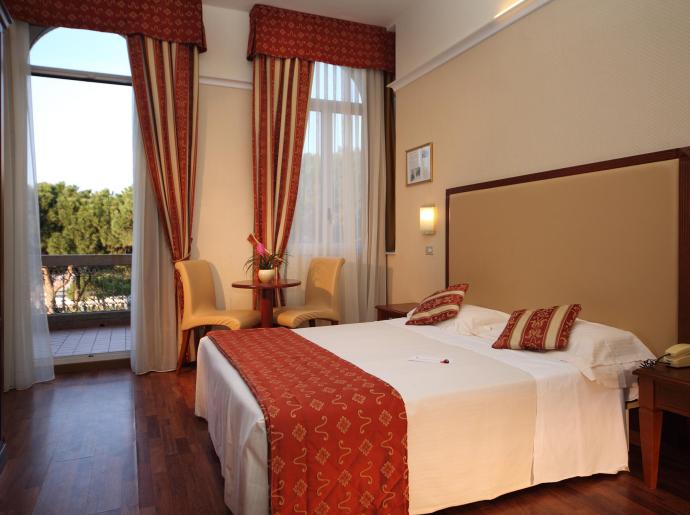 Camera d'albergo con letto matrimoniale, balcone e arredi eleganti.