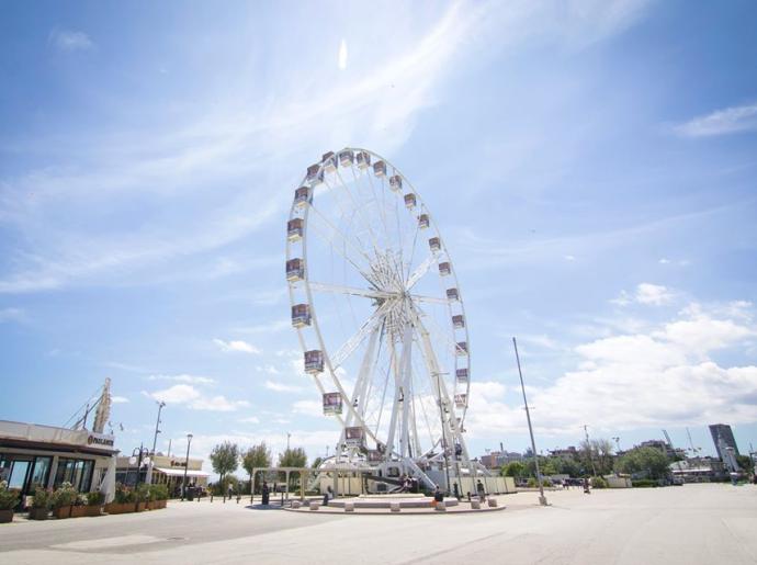 Ruota panoramica in una piazza soleggiata con cielo azzurro.
