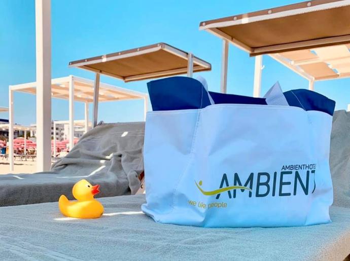 Borsa bianca su lettino da spiaggia con papera di gomma gialla.