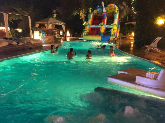 Nachtpool mit aufblasbarer Rutsche und schwimmenden Personen.
