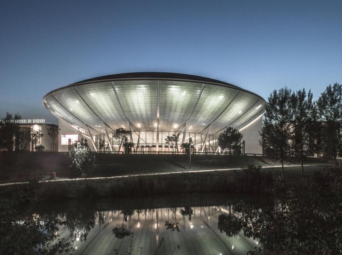 Centro congressi moderno con tetto illuminato, riflesso nell'acqua.