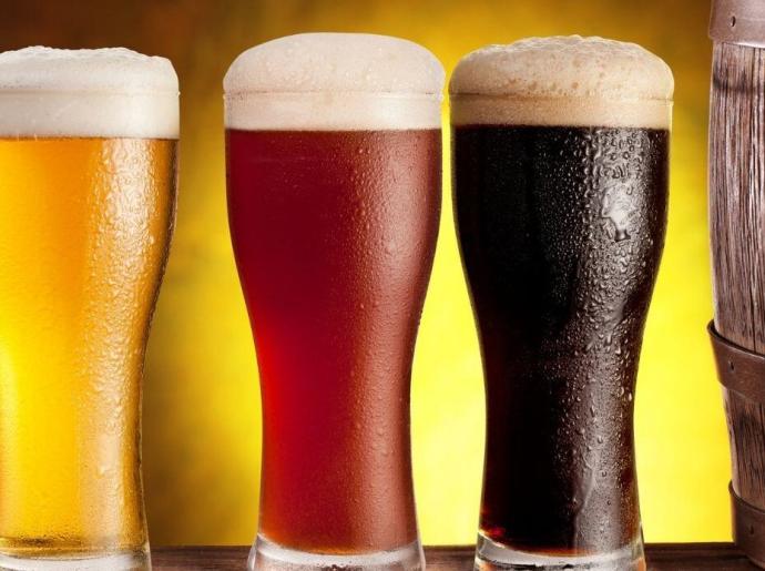 Tre bicchieri di birra chiara, ambrata e scura accanto a una botte.