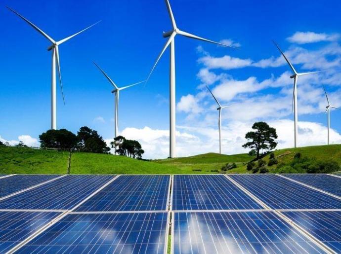 Pannelli solari e turbine eoliche su colline verdi sotto cielo blu.