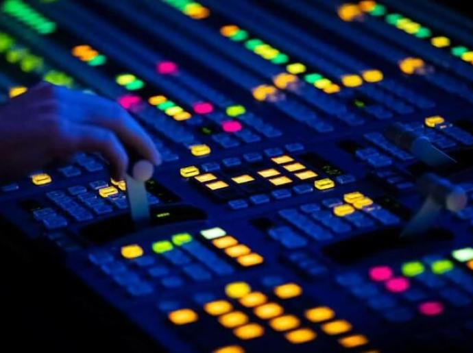 Mani che regolano una console di mixaggio audio illuminata.