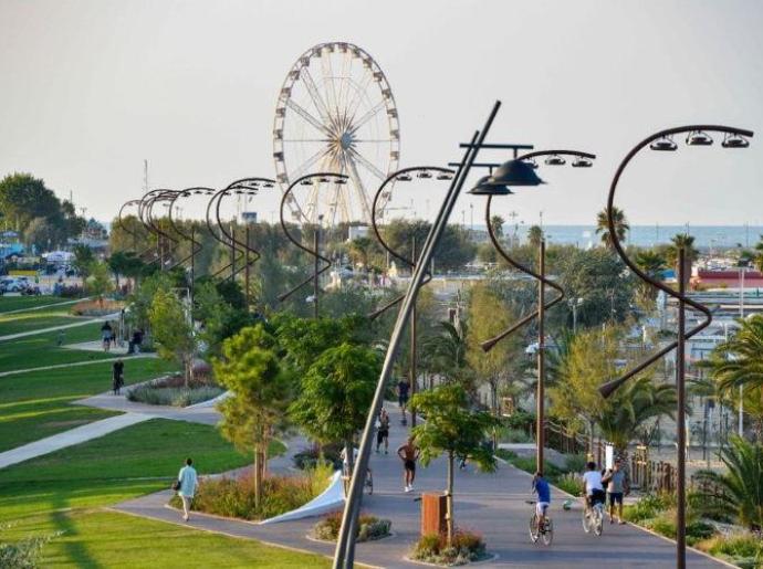 Parco urbano con ruota panoramica e pista ciclabile vicino al mare.