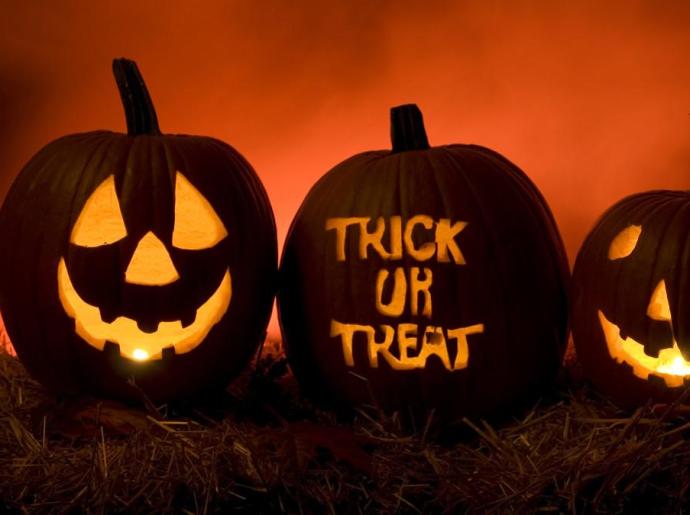 Drei geschnitzte Kürbisse mit Kerzen: zwei lächelnde Gesichter und 'Trick or Treat'.