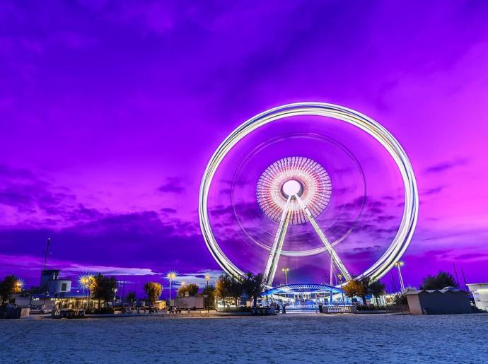 Ruota panoramica illuminata con cielo viola al tramonto.