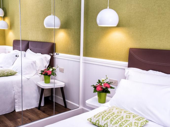 Camera da letto moderna con pareti verdi, lampade bianche e fiori sul comodino.