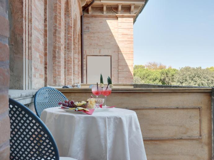 Terrazza con tavolo apparecchiato, drink e frutta, vista su alberi.